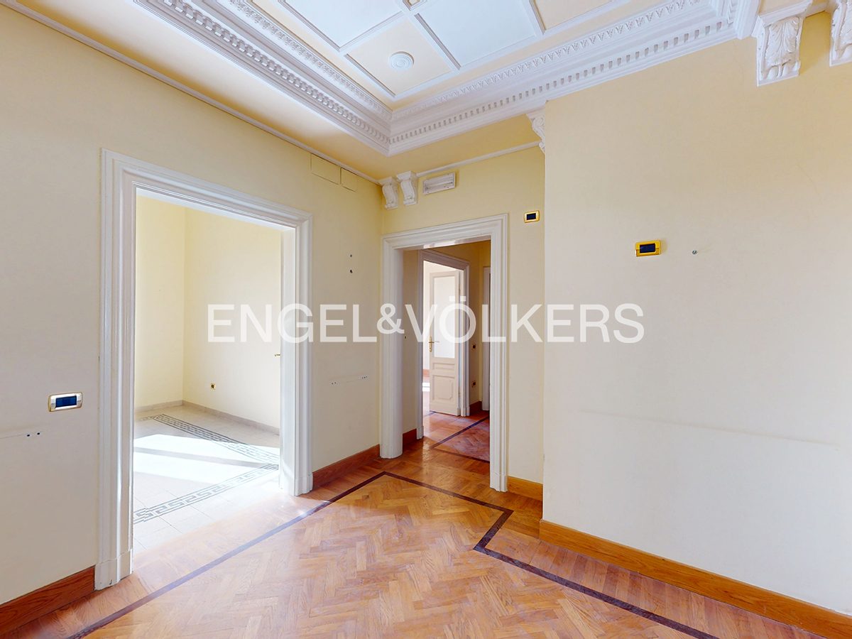 Bright hallway with cream walls, ornate crown molding, and polished herringbone wood flooring leading to adjacent rooms.
