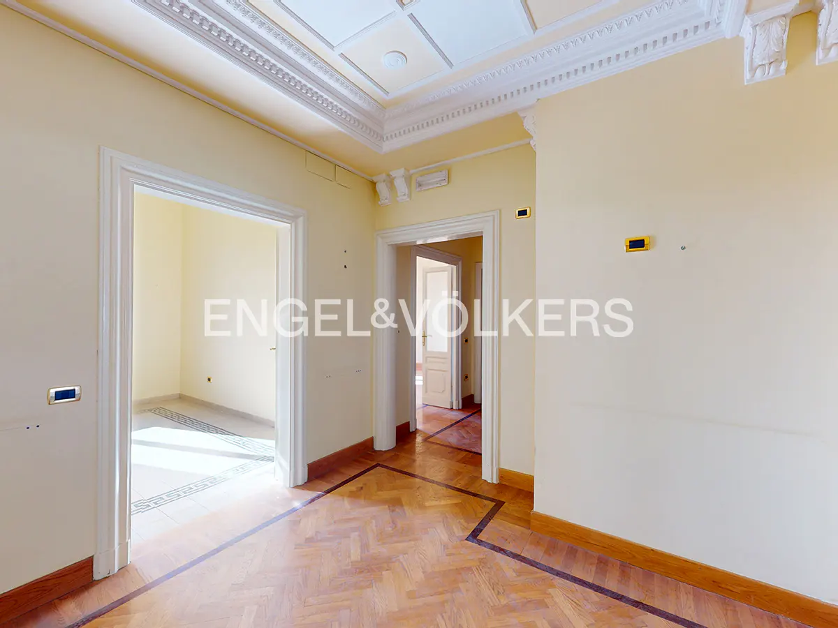 Bright hallway with cream walls, ornate crown molding, and polished herringbone wood flooring leading to adjacent rooms.