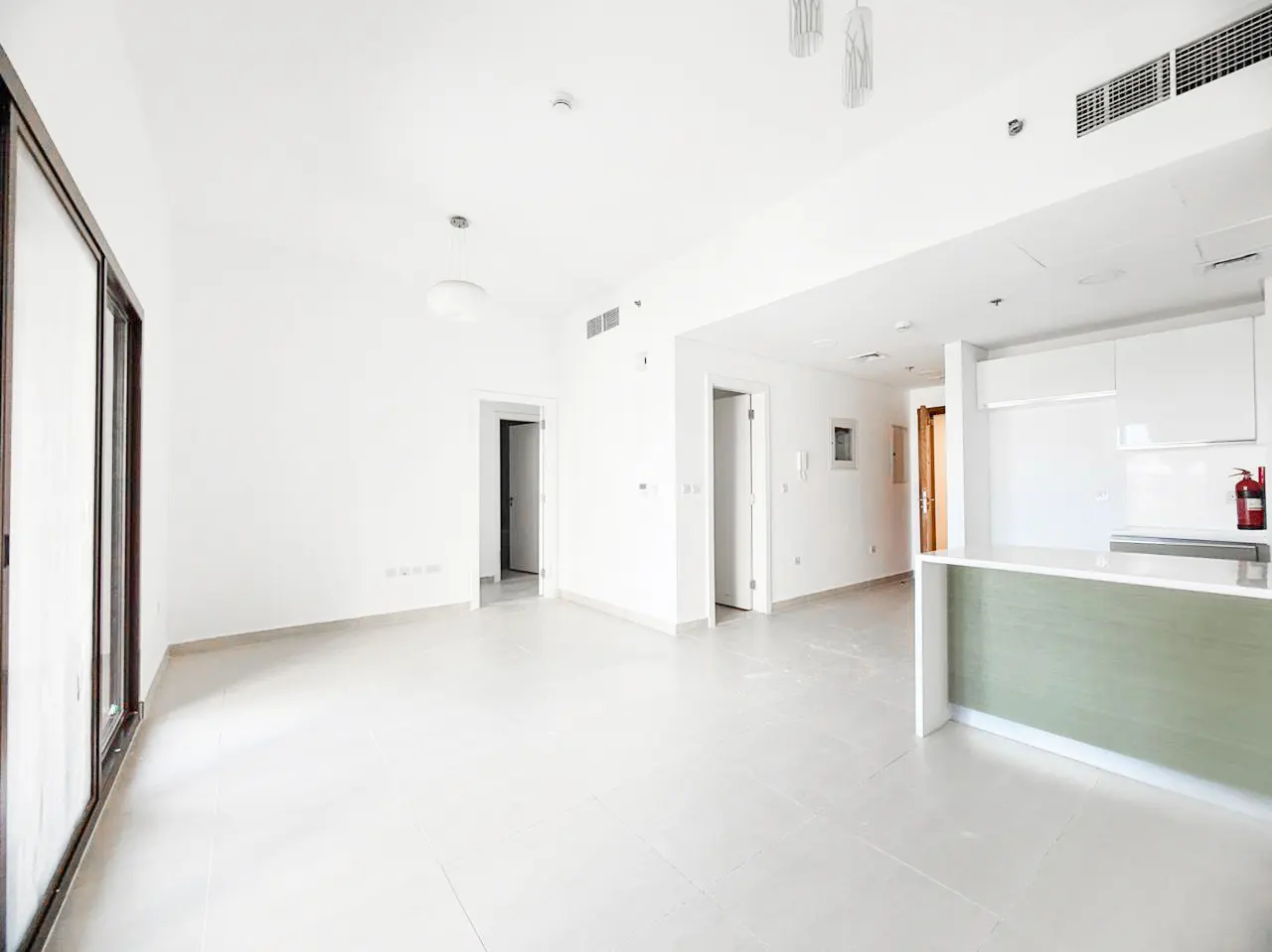 Bright, open-plan living area with white walls, tiled floors, and a modern kitchen featuring a light green island.