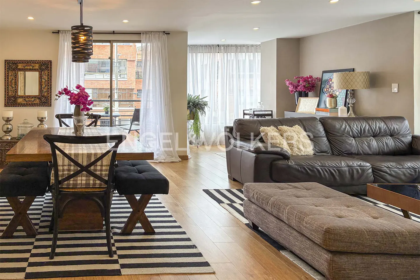 Open-concept living and dining area with wood floors, a brown leather sofa, and a striped rug.