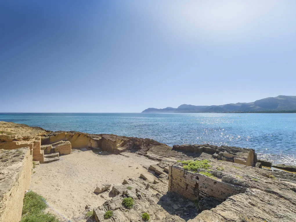 Coastal view of turquoise sea meeting a sandy beach with rocky formations under a clear blue sky.