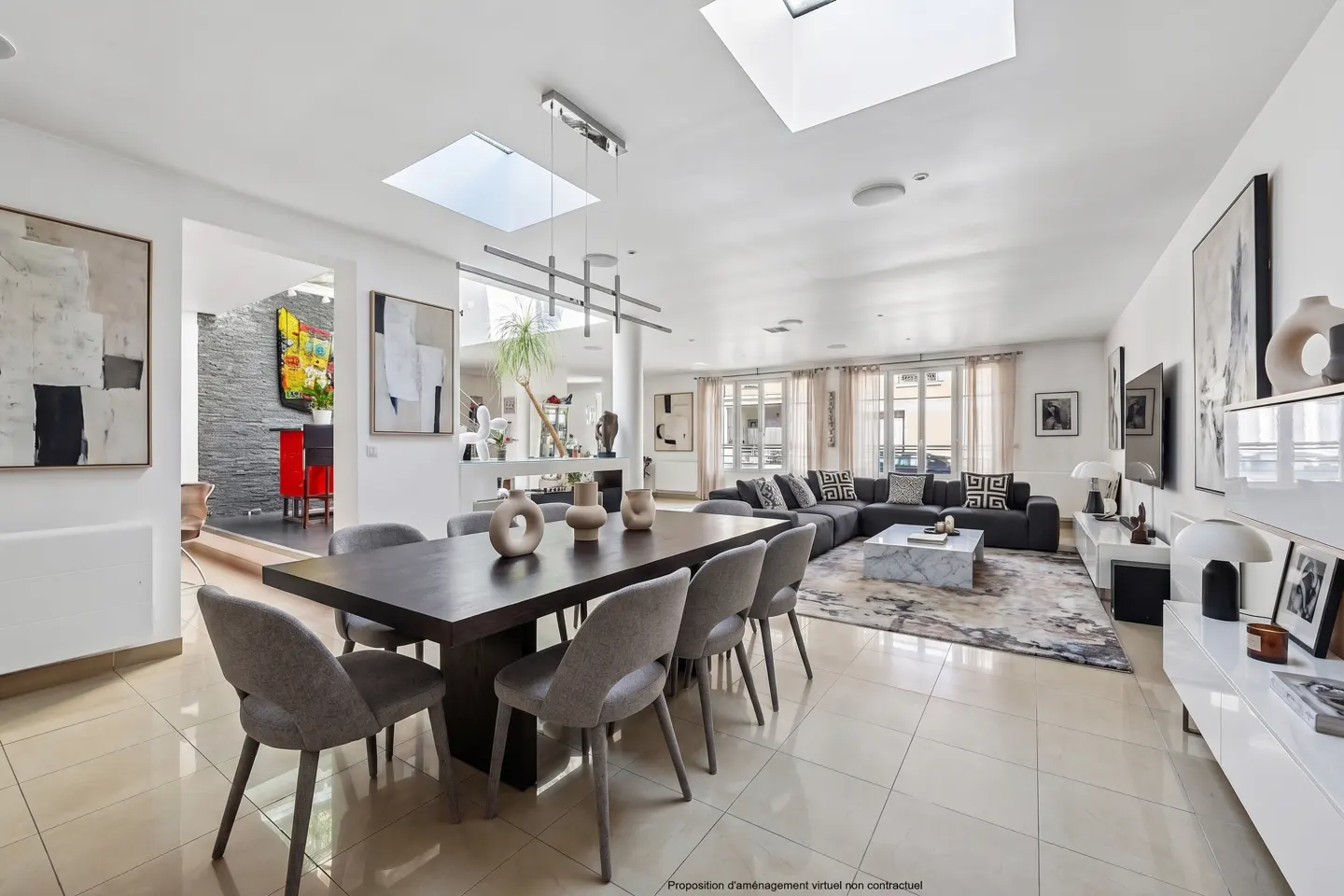 Bright, open-concept living and dining area with a dark wood table, gray chairs, and skylights. A gray sectional sofa is in the background.