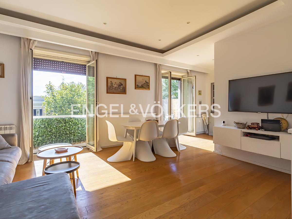 Bright living room with hardwood floors, white dining set, modern TV console, and balcony access with green views. [AI-generated text]