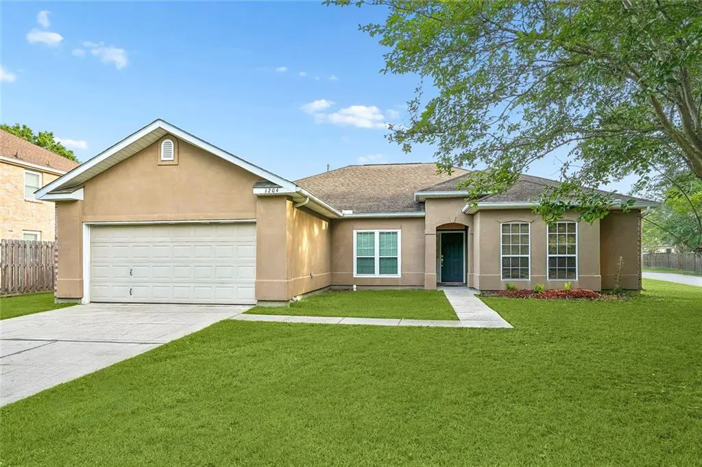 Beige single-story home with a two-car garage, green lawn, and a dark green front door under a blue sky.