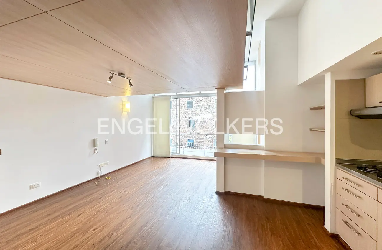 Wide shot of a modern apartment interior with wood floors, white walls, and a balcony view of a brick building.