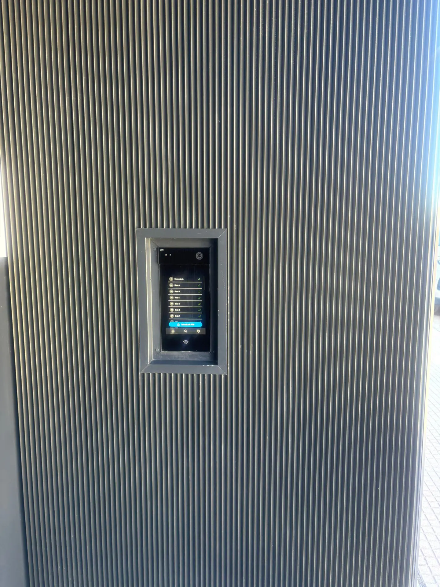 A gray, vertically ribbed wall with a small, recessed digital display showing a menu with blue highlights.