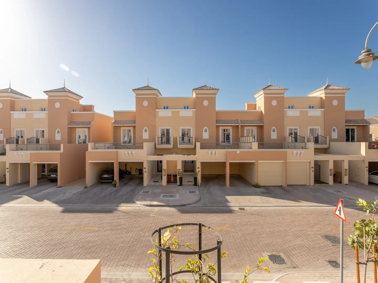 Row of tan townhouses with garages under a blue sky. A brick road runs in front of the houses.
