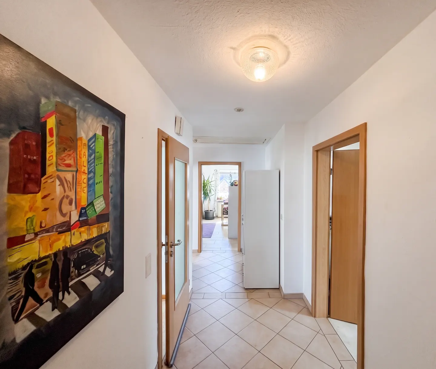 Hallway with beige tile floor, white walls, and wood doors. A colorful city painting hangs on the left wall.