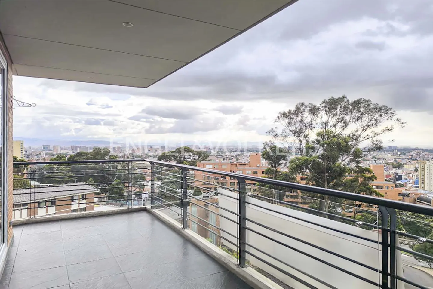 Balcony view with black metal railings overlooking a cityscape under a cloudy sky.
