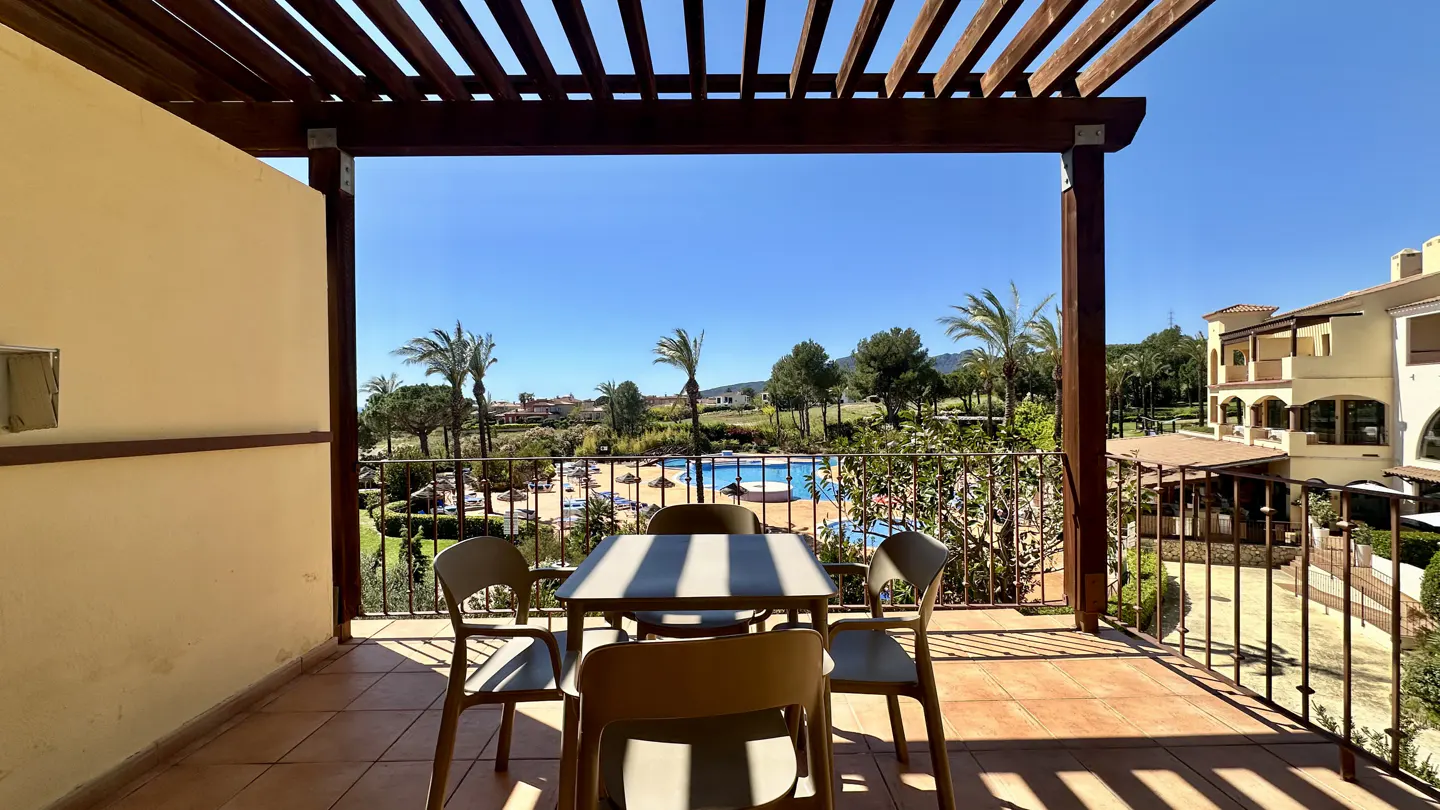 Balcony view with table and chairs overlooking a pool and palm trees under a clear blue sky.