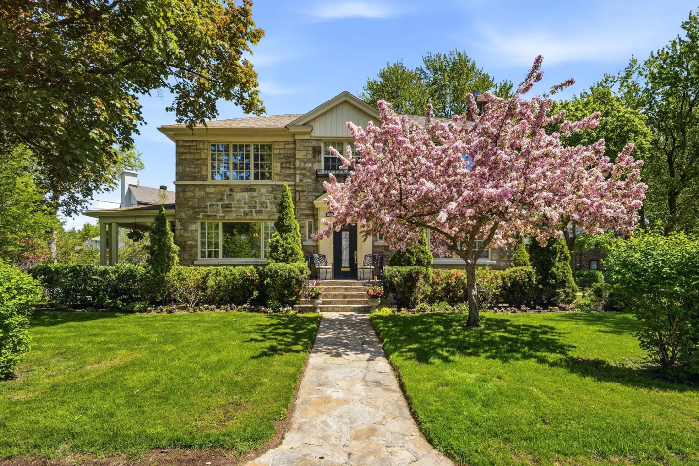 Stone house with a pink flowering tree in the front yard on a sunny day. Stone walkway leads to the front door.