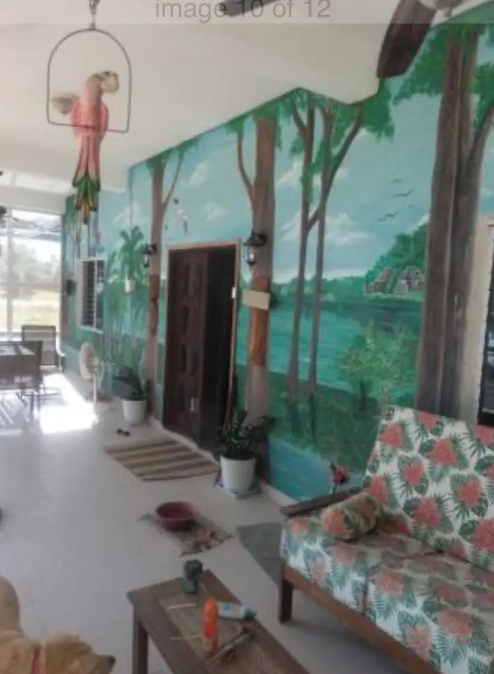 A sunroom with a mural of a lake and trees, a pink parrot in a cage, and a floral sofa.