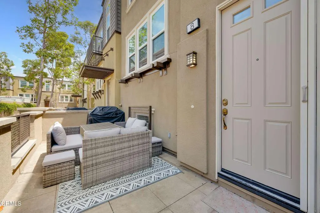 Exterior view of a condo patio with wicker furniture, a grill, and a beige front door with the number 8 on the wall.