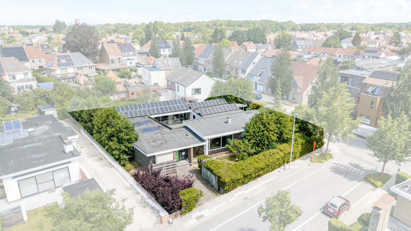 Aerial view of a modern flat-roof house with solar panels, surrounded by lush hedges in a quiet residential neighborhood.