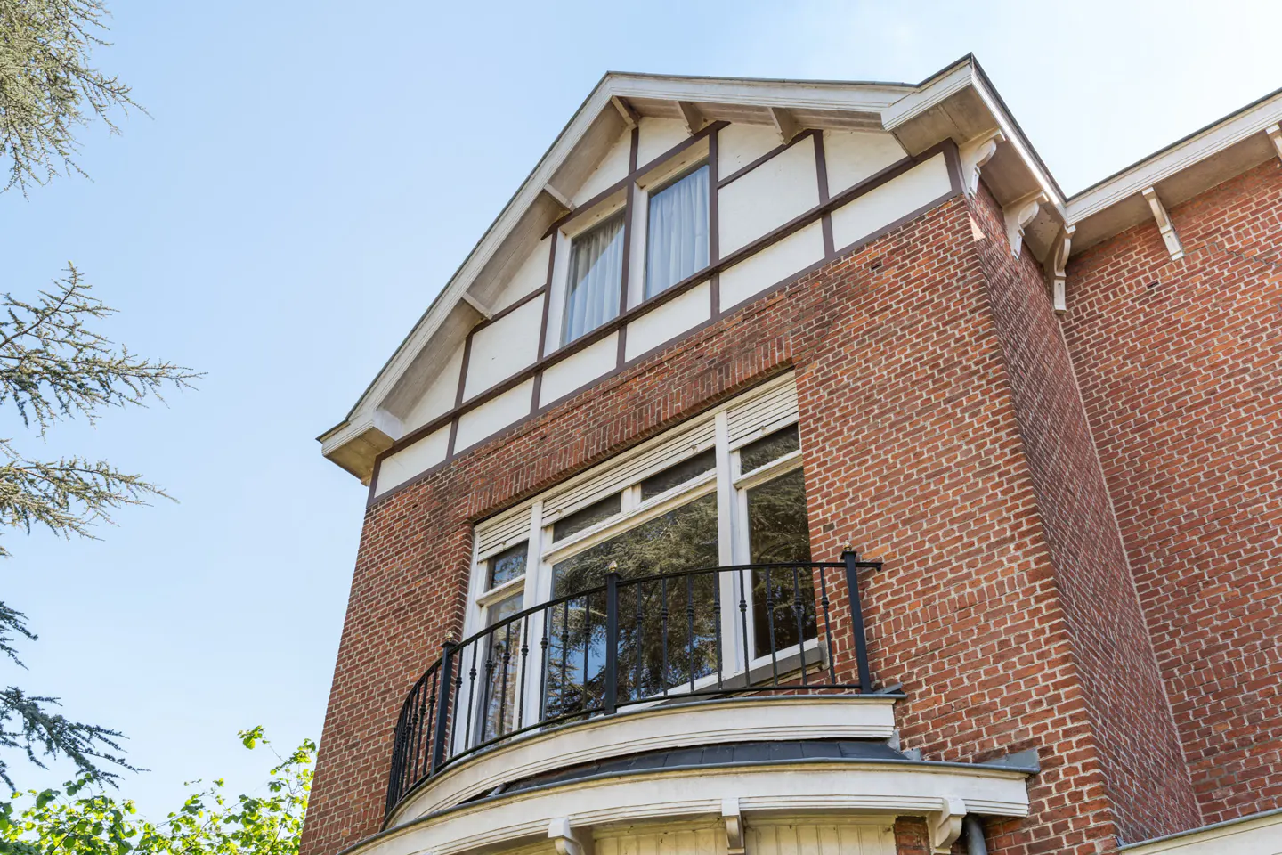 Exterior view of a two-story brick house with a balcony and white trim under a blue sky.