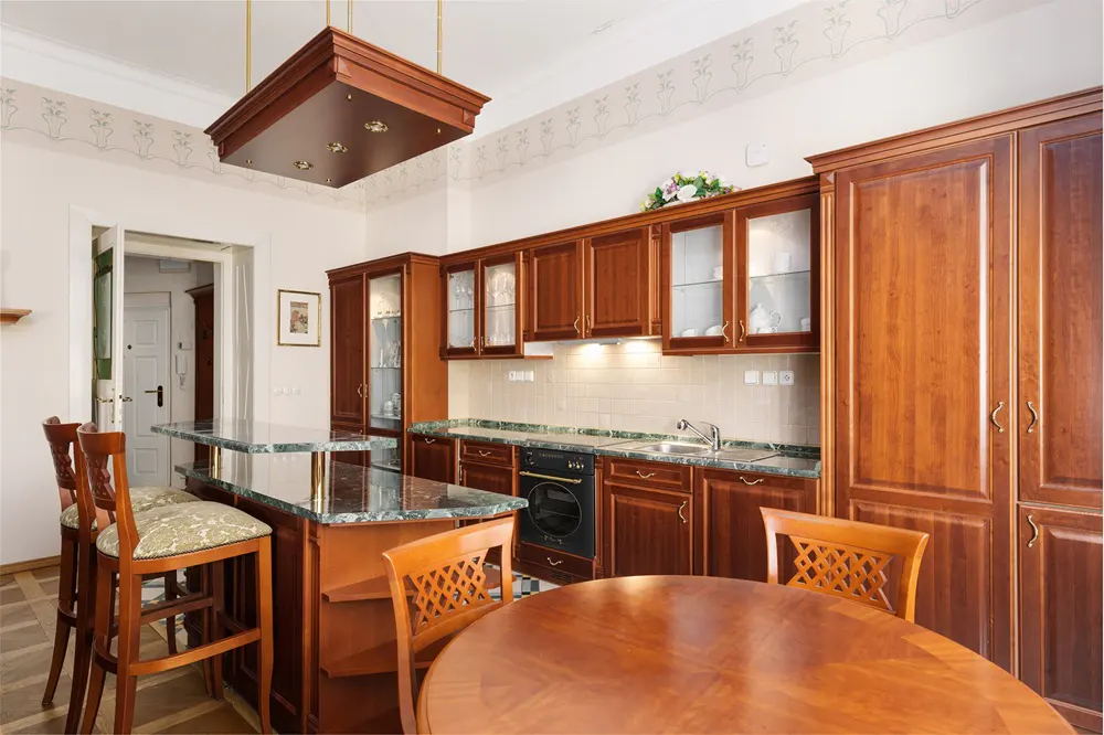 A kitchen with wood cabinets, a marble countertop island, and a round wood table.