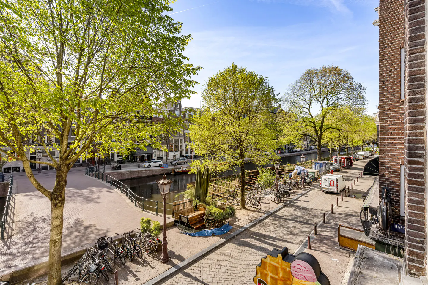 View of an Amsterdam canal lined with trees, bikes, and buildings on a sunny day.