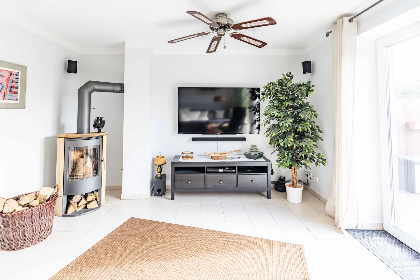 Bright living room with a wood-burning stove, TV, dark console table, and a brown rug on a white floor.