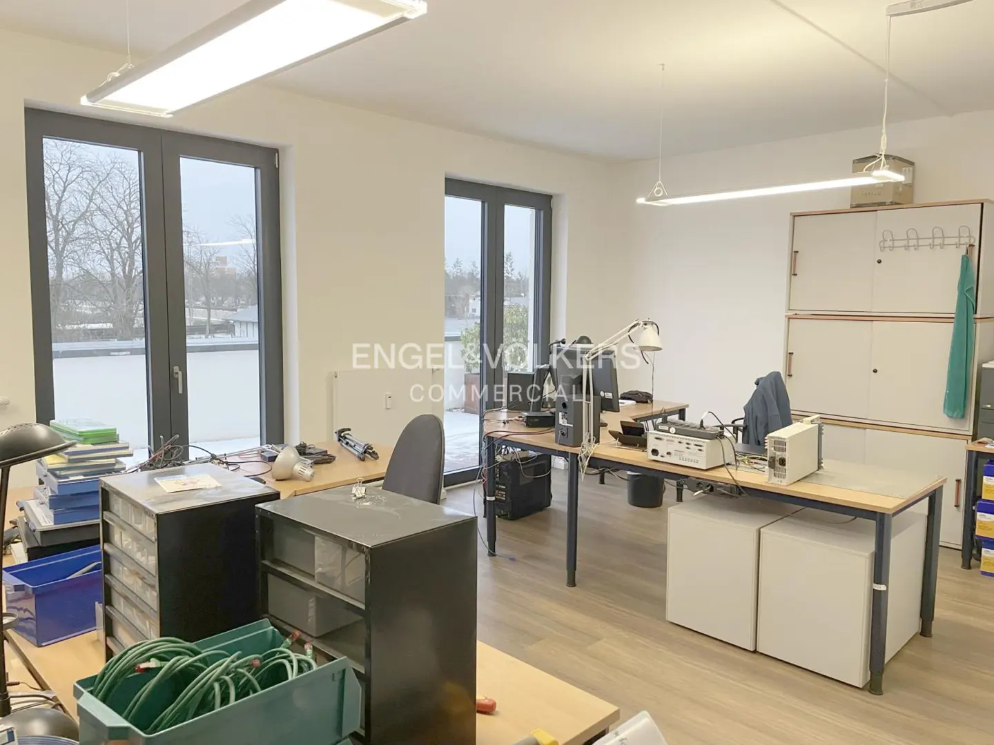 Bright office space with desks, storage cabinets, and large windows. The Engel & Völkers Commercial logo is visible on the wall.