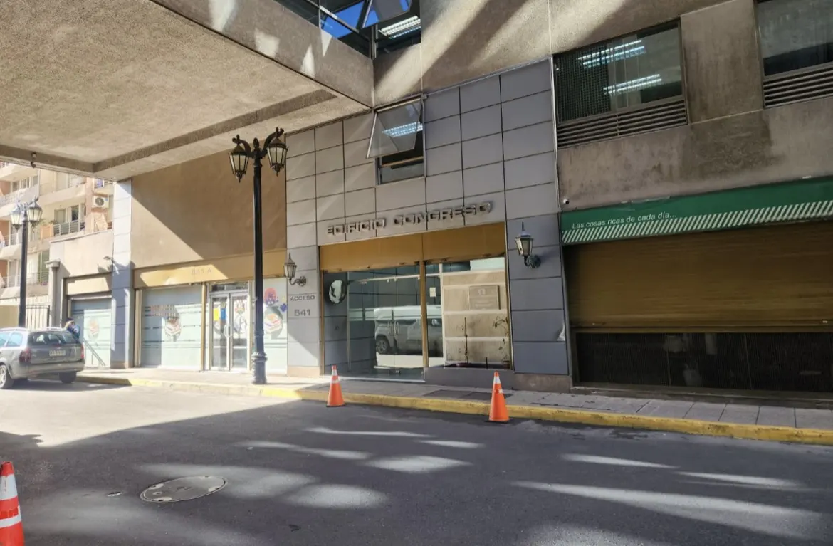 Exterior view of Edificio Congreso, a gray building with a glass entrance, street lamps, and orange cones.