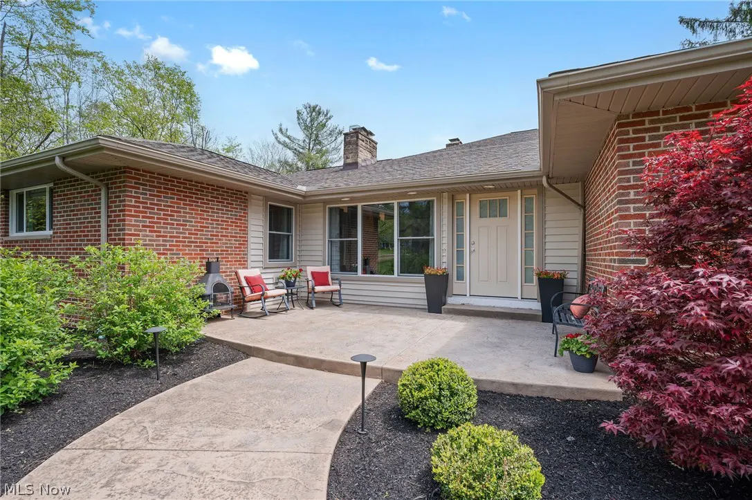 Exterior view of a single-story brick and siding home with a concrete patio, chairs, and landscaping.