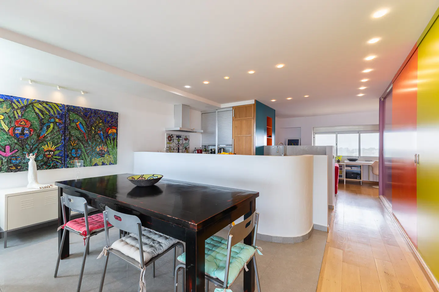 Bright, modern apartment interior with a black dining table, colorful art, and an open kitchen.