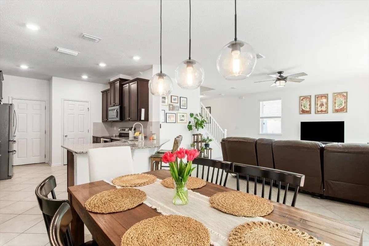 A bright, open-concept home interior with a dining table set for six, featuring red tulips. The kitchen and living room are visible in the background.