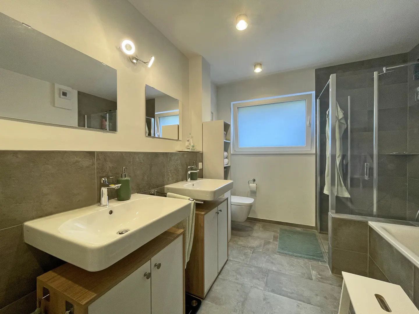 Bathroom with two white sinks, gray tile floor, toilet, and shower with glass door.