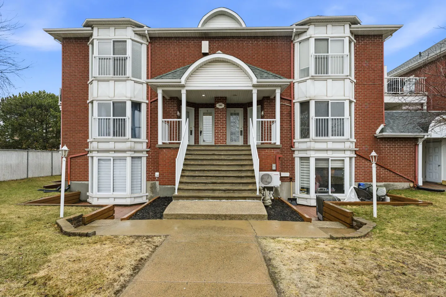 Exterior view of a two-story red brick apartment building with white trim and a central staircase leading to two front doors.