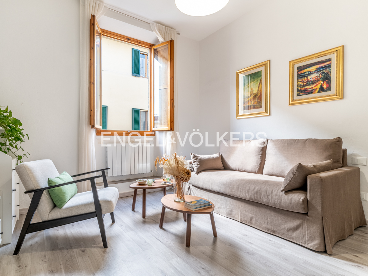 Bright living room with a beige sofa, white armchair, two wooden coffee tables, and framed art on white walls. [AI-generated text]