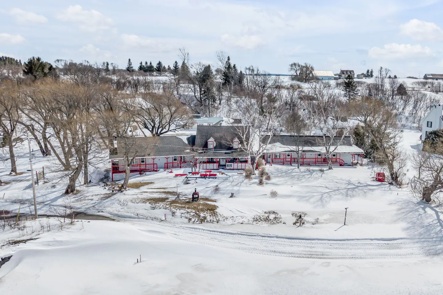 Aerial view of a white building with red trim, surrounded by snow-covered ground and bare trees.