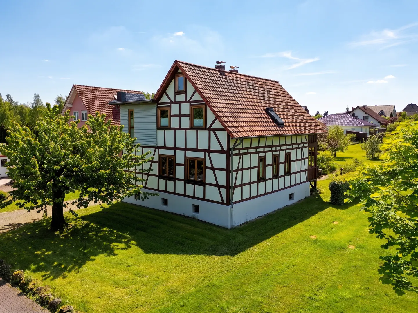 Two-story half-timbered house with a red tile roof and green lawn on a sunny day.