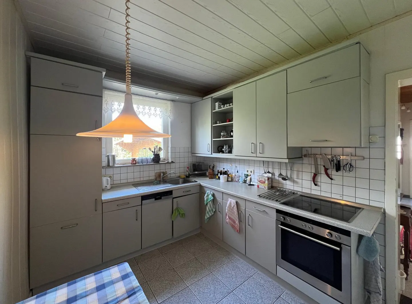 A bright kitchen with gray cabinets, white tile backsplash, and a large, white pendant light.