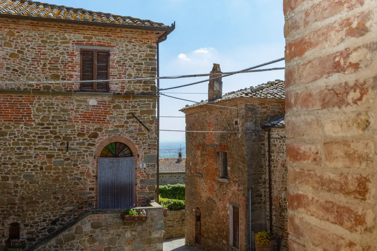 A narrow street view of old stone buildings in Tuscany, Italy, with a blue sky above.