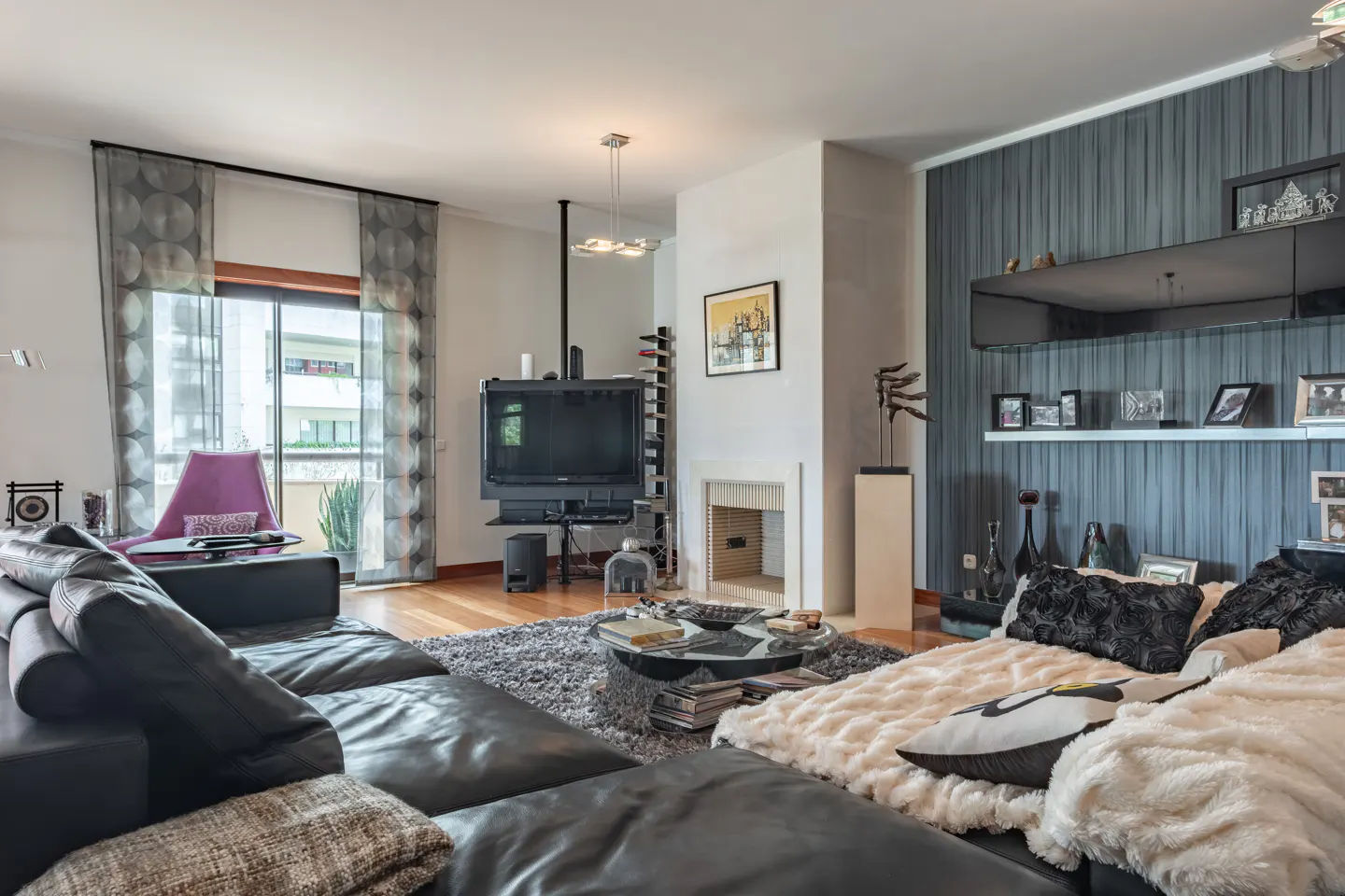 Living room with a black leather sectional sofa, gray rug, TV, fireplace, and a shelf with photos.