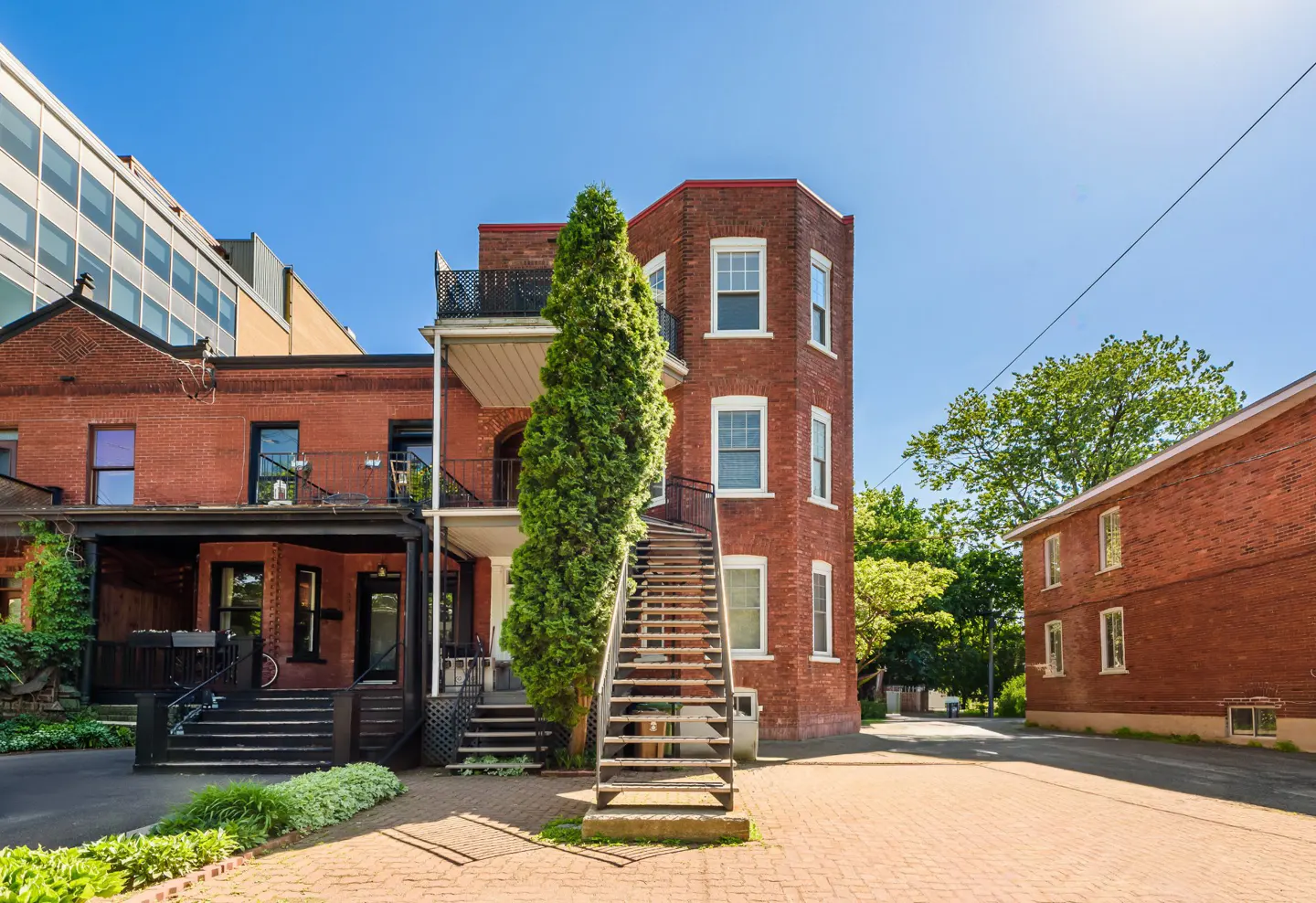 Exterior view of a red brick apartment building with a metal staircase and balconies on a sunny day.