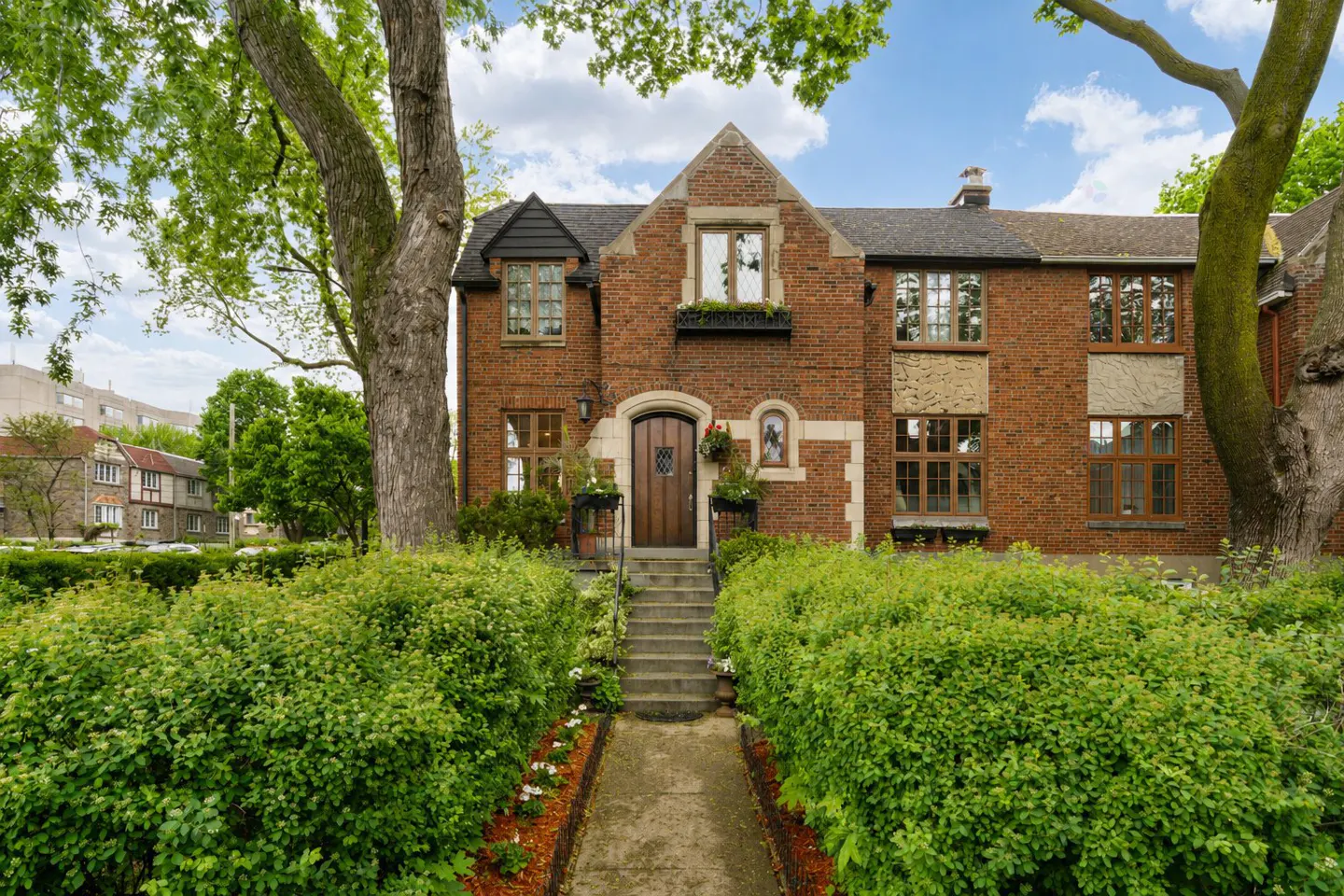 A two-story brick house with a brown front door and green bushes in the front yard.