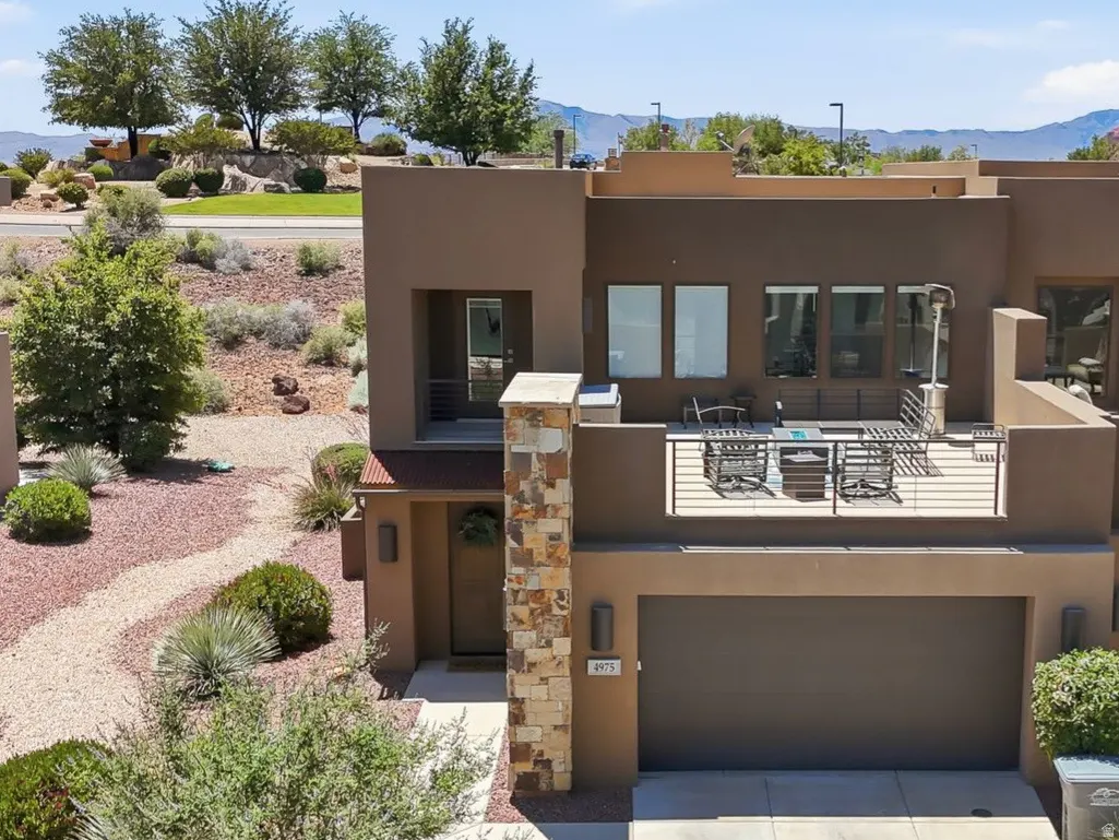 Modern brown two-story home with a stone pillar, second-floor patio, and desert landscaping against a mountain backdrop.