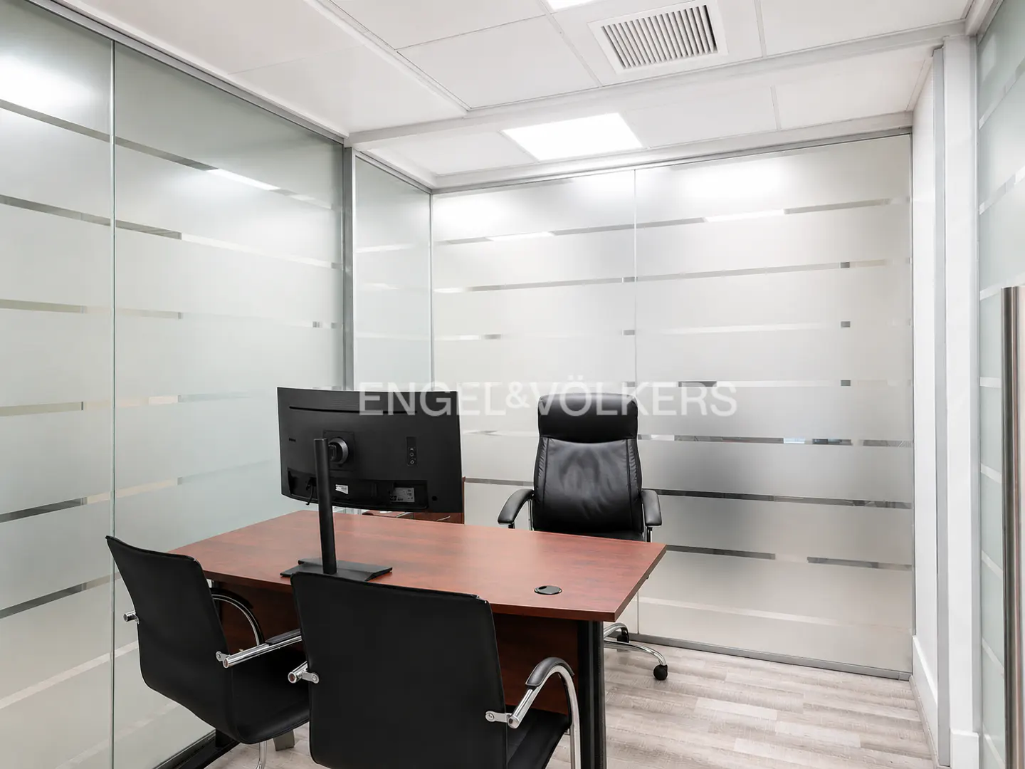 Office space with frosted glass walls, a wood desk, black chairs, and a computer monitor.