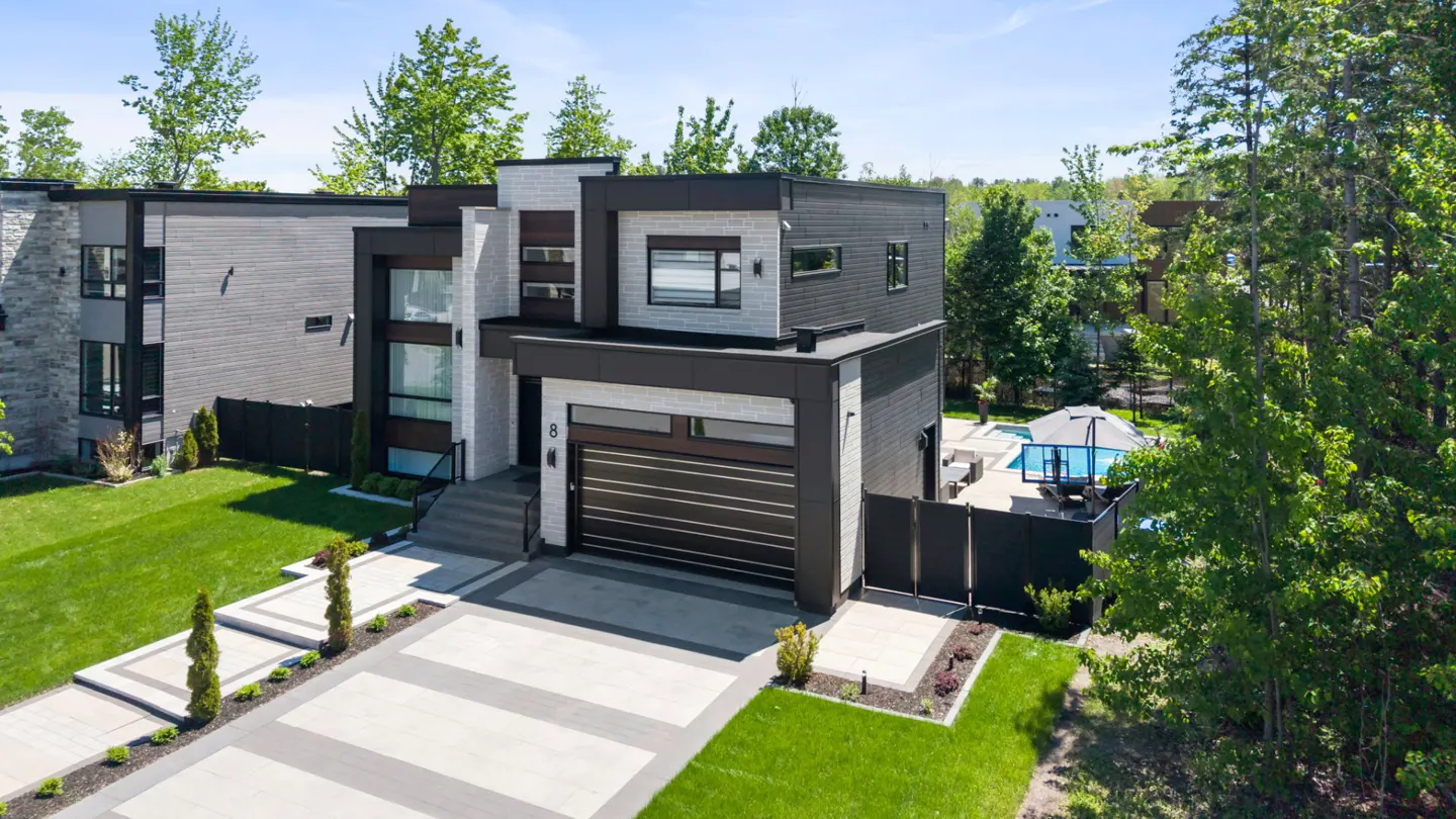 Modern two-story home with black and white exterior, a garage, paved driveway, and a backyard pool on a sunny day.