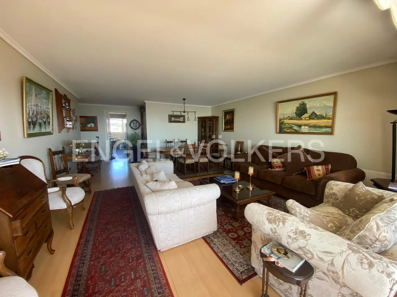 A wide shot of a living room with sofas, a dining table, and paintings on the wall.