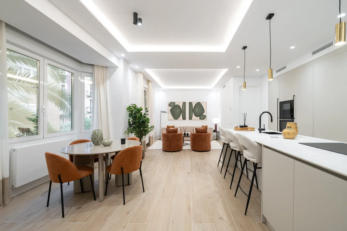Bright, open-concept living space with a dining table, kitchen island, and seating area. The color palette is neutral with orange accents.