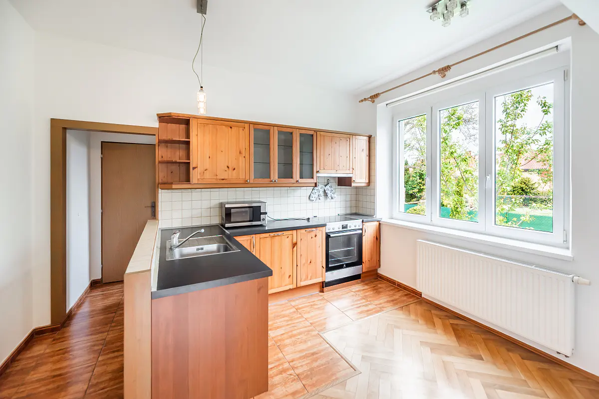 Bright kitchen with wood cabinets, black countertops, and a stainless steel sink. A large window overlooks a green yard.