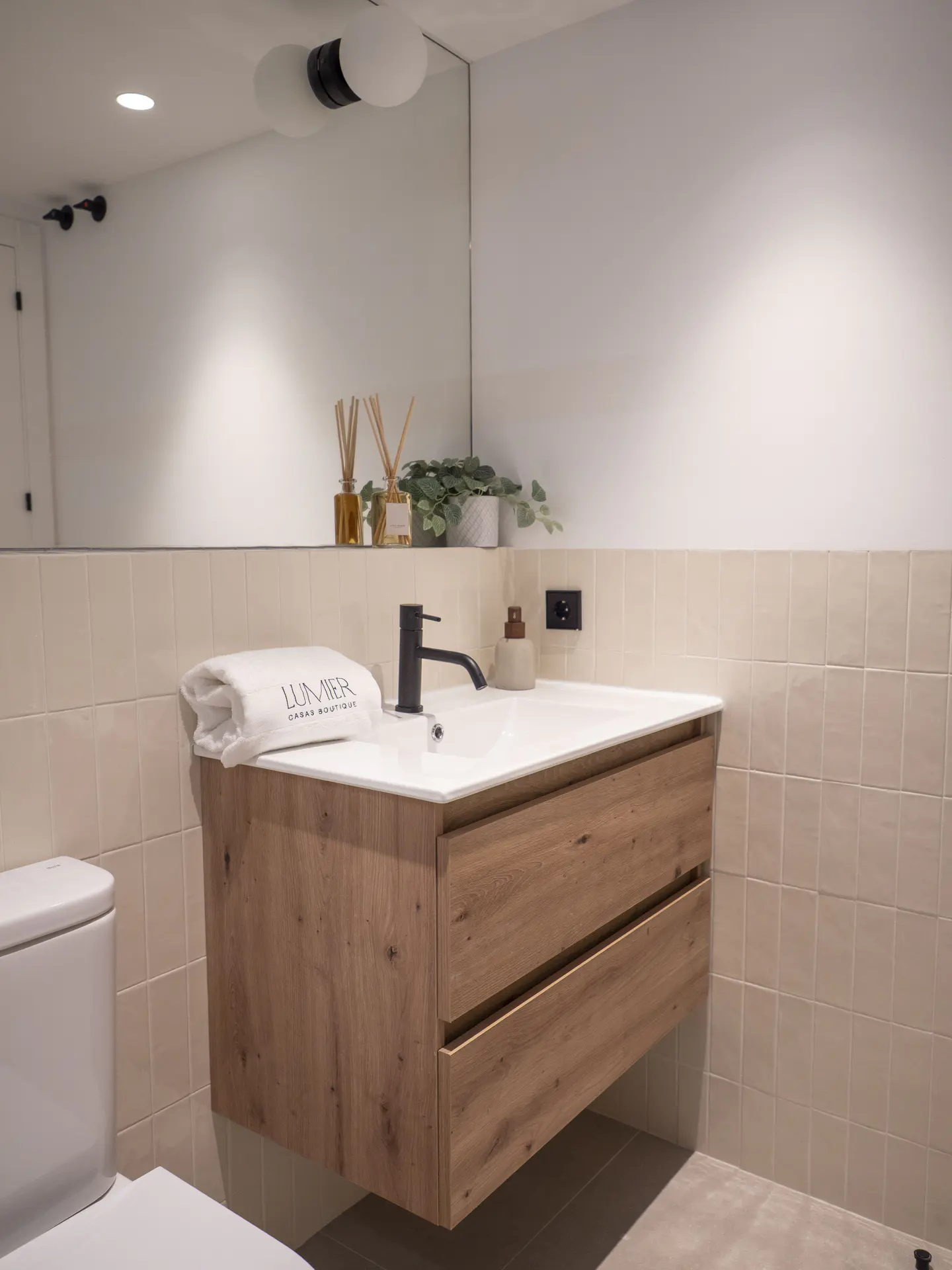 Bathroom with a floating wood vanity, white countertop, black faucet, and a white towel. A toilet is visible on the left.