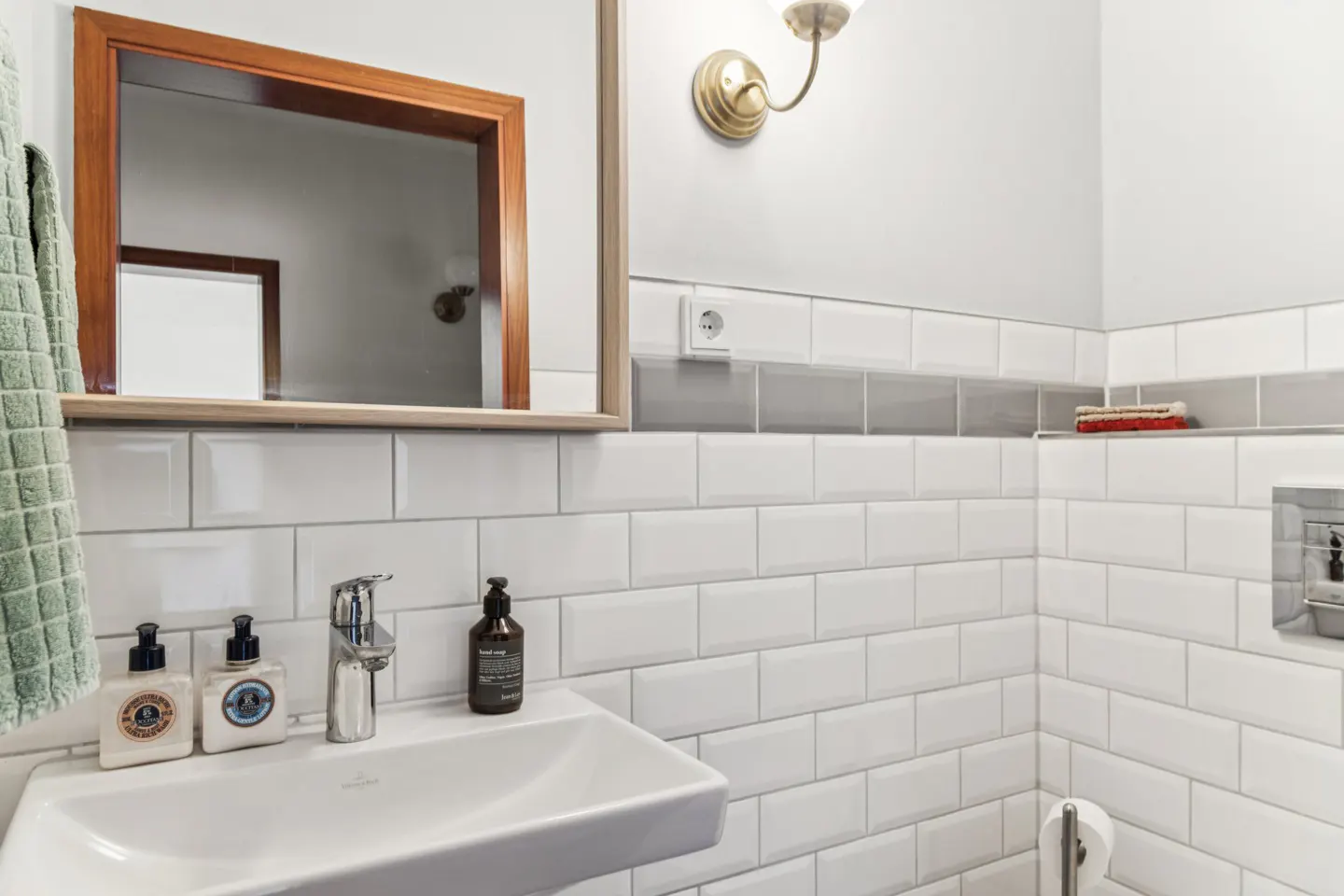 Bathroom with white subway tile, a white sink with toiletries, and a wood-framed mirror.