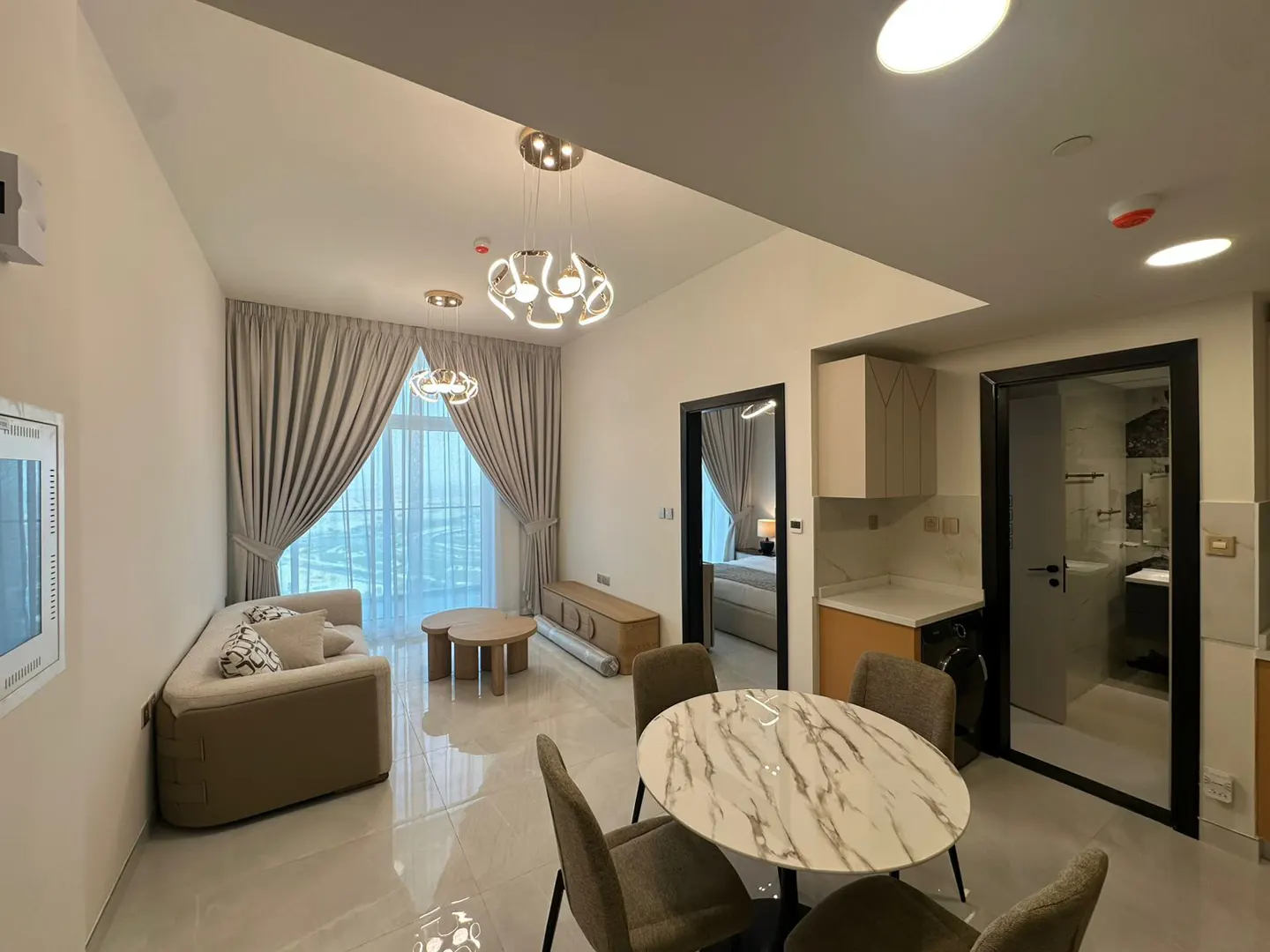 A modern apartment interior with a round marble table, chairs, sofa, and large window with beige curtains.