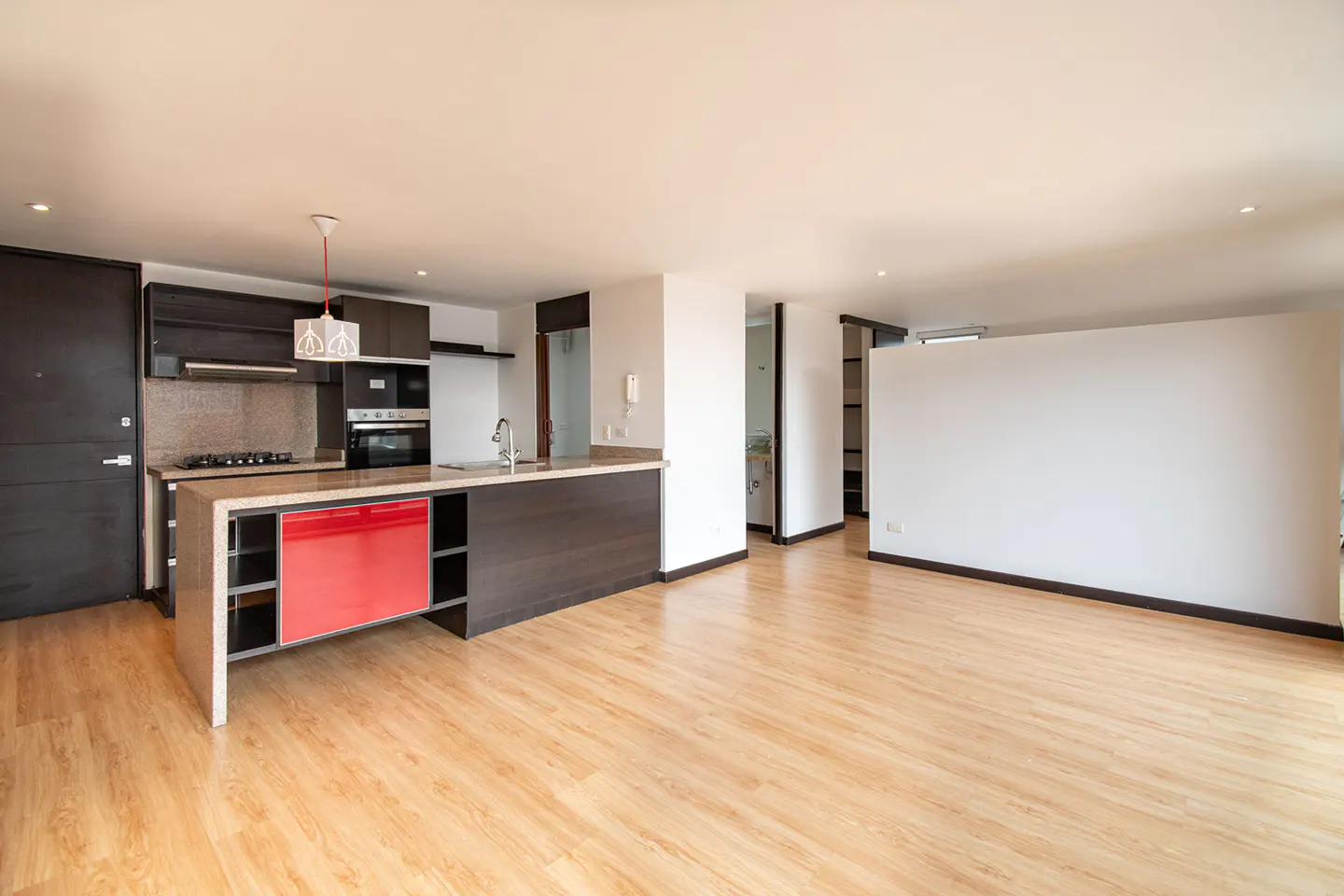 Open-concept apartment with wood floors, a kitchen island with red accents, and dark cabinets.