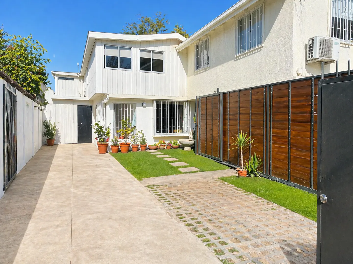 Exterior of a two-story white house with a driveway, lawn, and wooden fence under a blue sky.