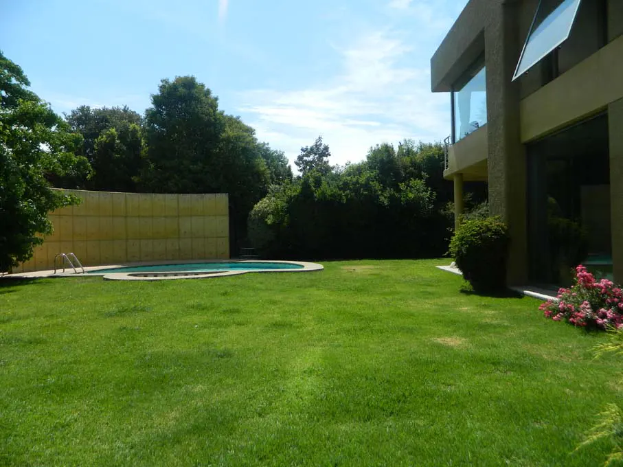 A backyard with a pool, green grass, trees, and a modern house with large windows.