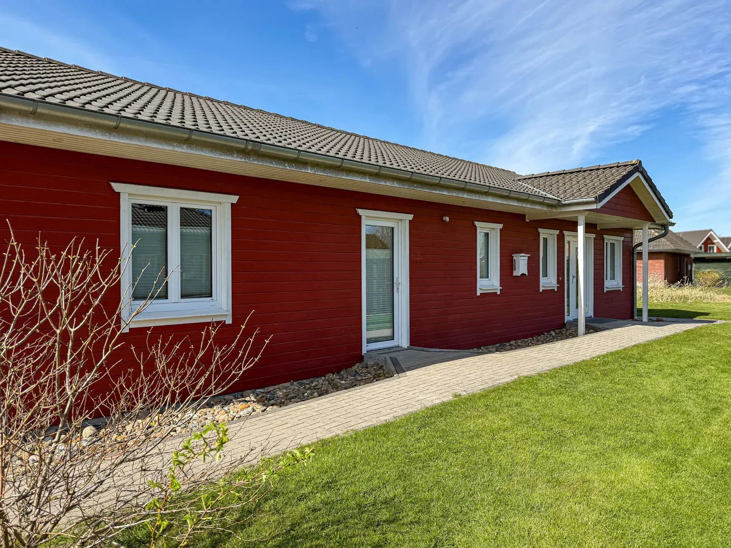 Red, one-story house with white trim, a gray roof, and a brick walkway on a sunny day.